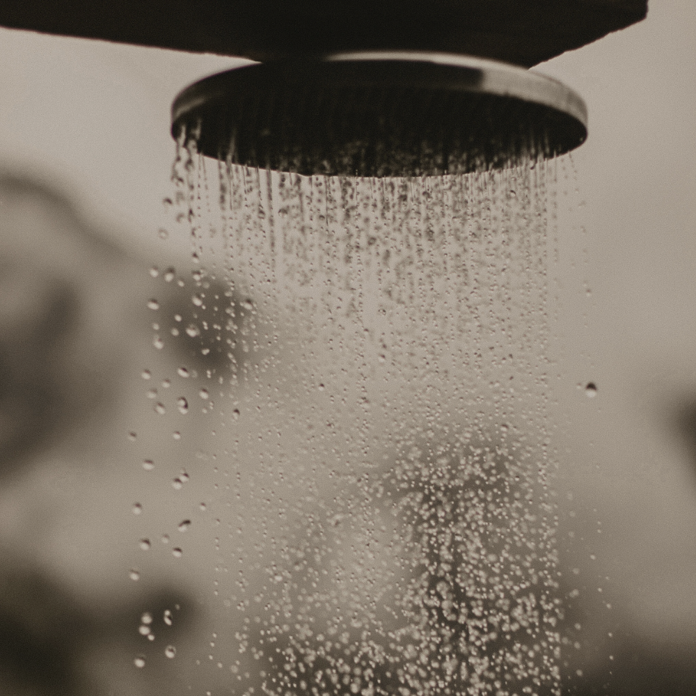 Close-up of a showerhead with water droplets cascading down in a blurred, soft-focus background, creating a serene atmosphere.