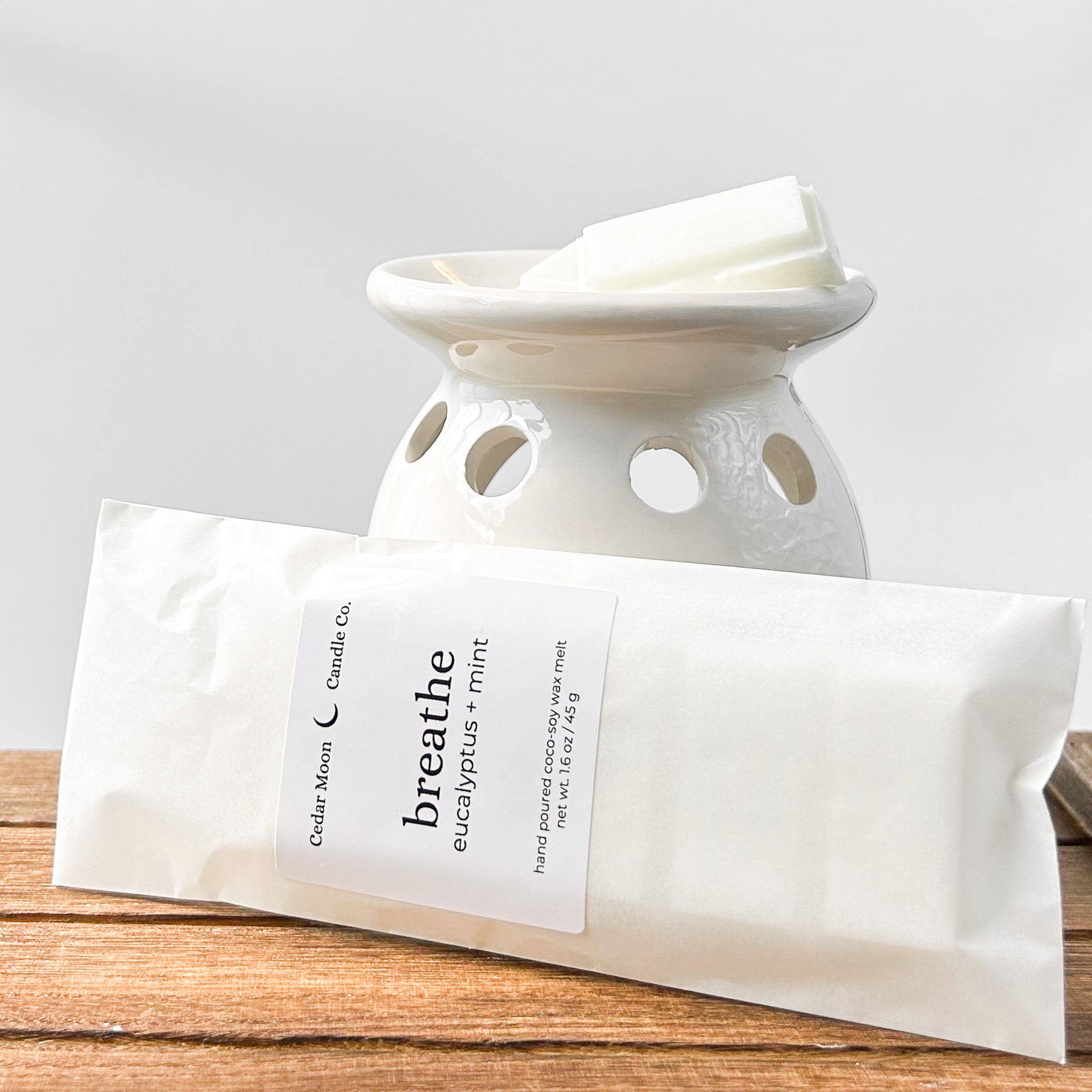 A ceramic wax warmer with white wax melts labeled 'breathe' in eucalyptus and mint scent, placed on a wooden surface.