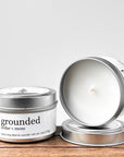 Two silver tins of 'grounded cedar and moss' coco-soy blend candle, one lid off, showcasing the white wax and wick. Placed on a wooden surface with a neutral background.