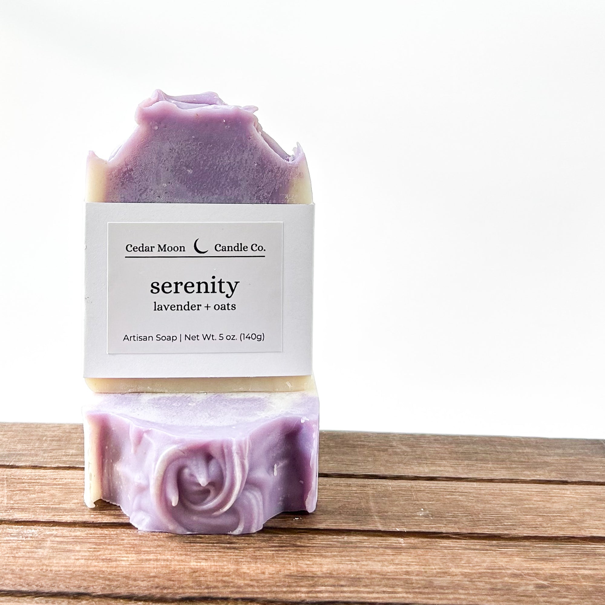 Artisan lavender and oats soap named 'Serenity' from Cedar Moon Candle Co., resting on a wooden surface with a small label detailing its contents.