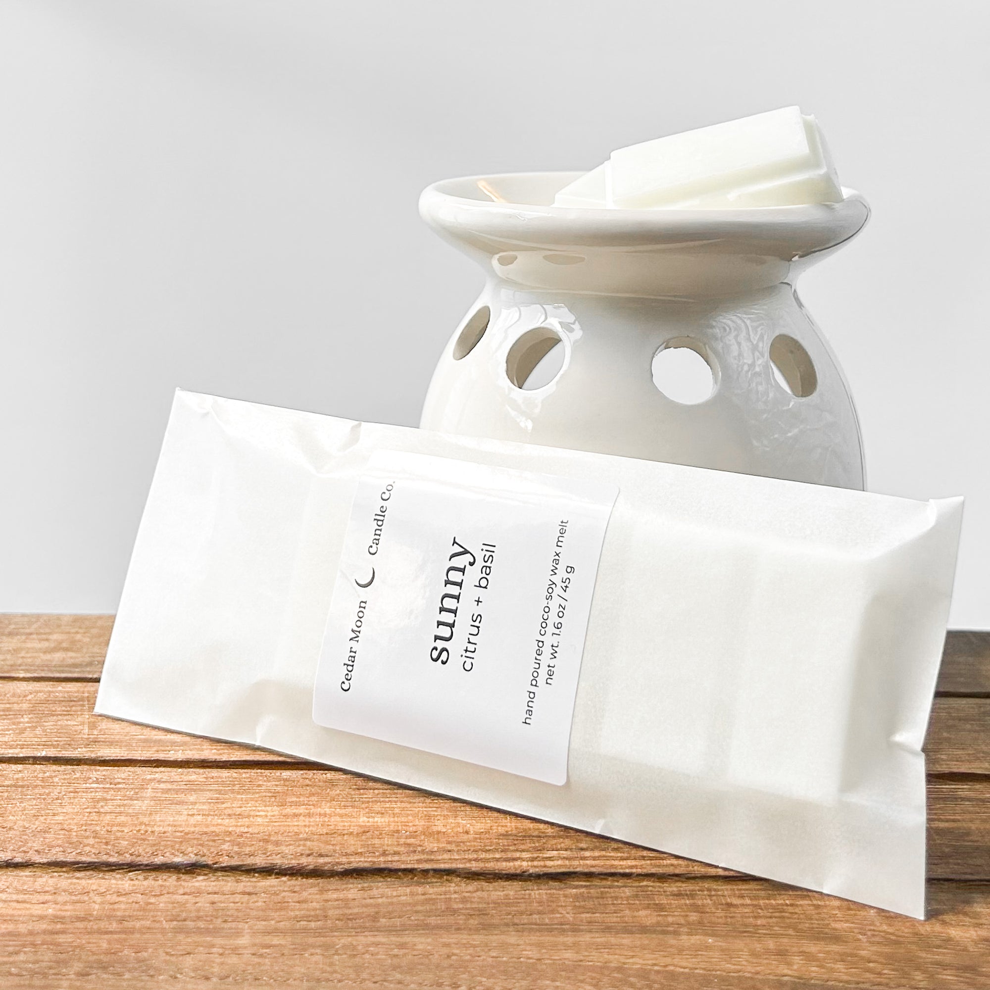 A ceramic wax warmer with white wax melts labeled 'sunny' in citrus and basil scent, placed on a wooden surface.