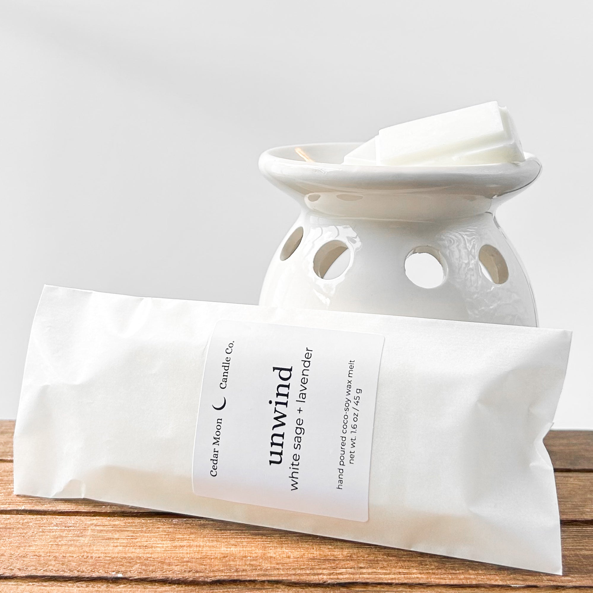 A ceramic wax warmer with white wax melts labeled 'unwind' in white sage and lavender scent, placed on a wooden surface.