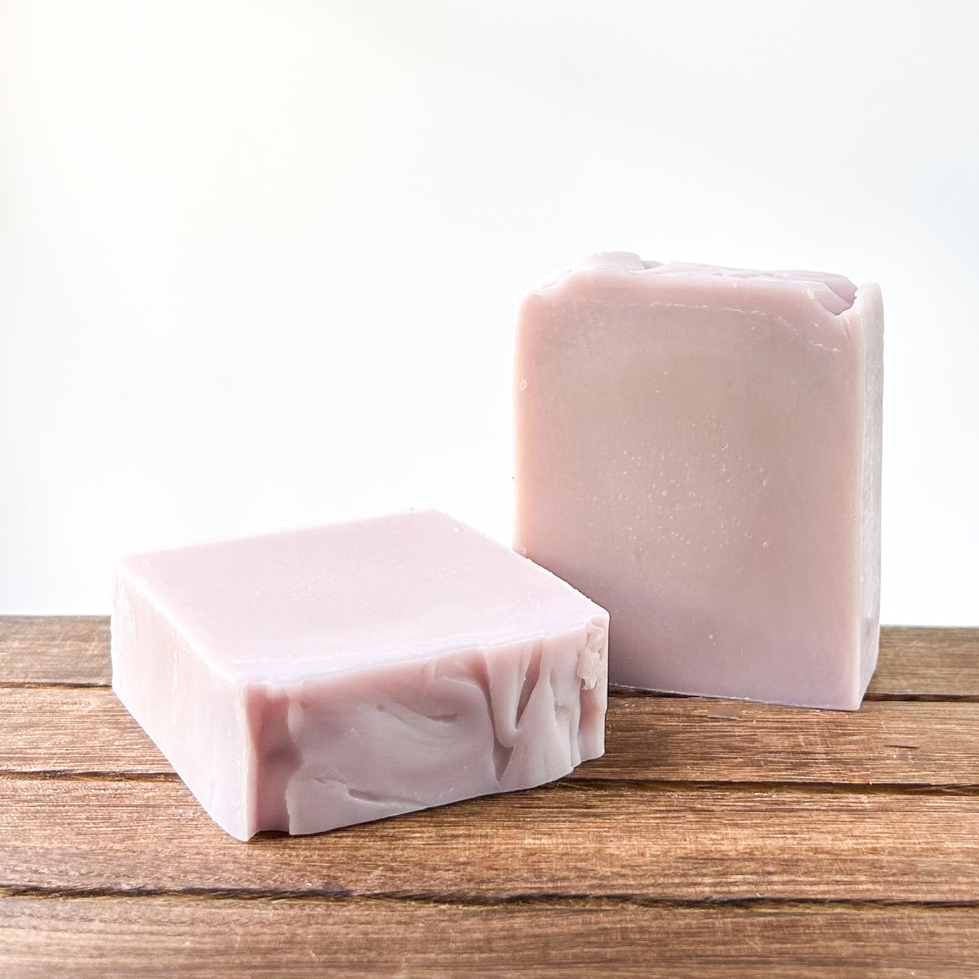 Two bars of pale purple marbled soap placed on a wooden surface, with a soft neutral background.