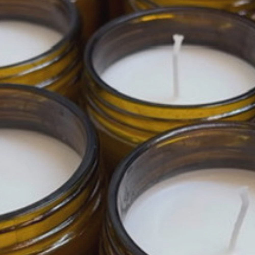 A close-up view of multiple amber glass candle jars filled with white wax, featuring cotton wicks peeking out at the center of each jar.